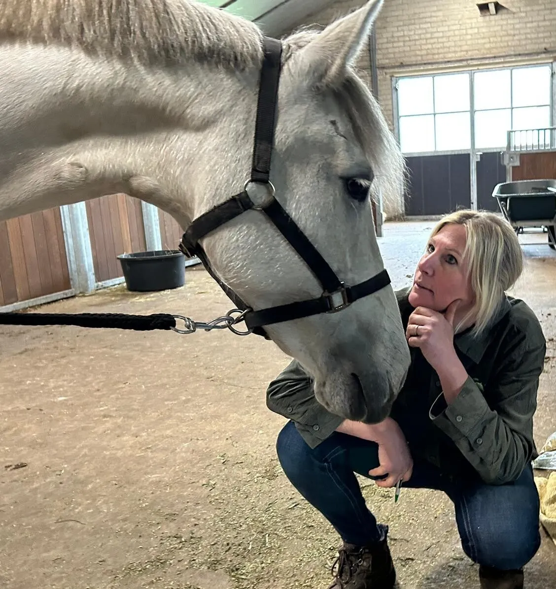 Angelique zit in stilte bij een witte pony op stal